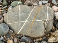Grauer Stein mit weißer Kreuzmaserung und rötlicher Binde